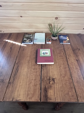 Une table en bois, sur laquelle se trouvent un carnet à spirales, une petite plante en pot et plusieurs livres.