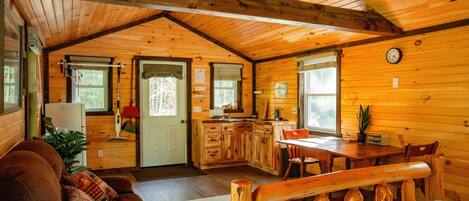 Un intérieur de chalet chaleureux comprenant un salon, une cuisine et un coin repas, avec des murs et des plafonds en bois.