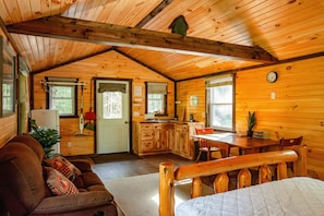 Interior acogedor de una cabaña con sala de estar, cocina y comedor, que presenta paredes y techos de madera.