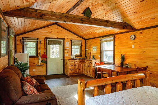 Un intérieur de chalet chaleureux comprenant un salon, une cuisine et un coin repas, avec des murs et des plafonds en bois.