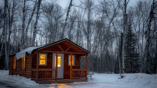 A wooden cabin with a porch, surrounded by a snowy forest.