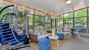 A sunroom with a swing chair, a sofa, and a dining area with a table and chairs. - Luxurious 4BD near Downtown and RDU, with sunroom, theatre, games, & more! (Raleigh)