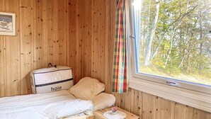 Une pièce en bois avec un lit, une valise et une fenêtre donnant sur des arbres.