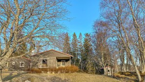 Un chalet rustique avec une façade en bois et un toit rouge, entouré d’arbres et d’un mur de pierres.