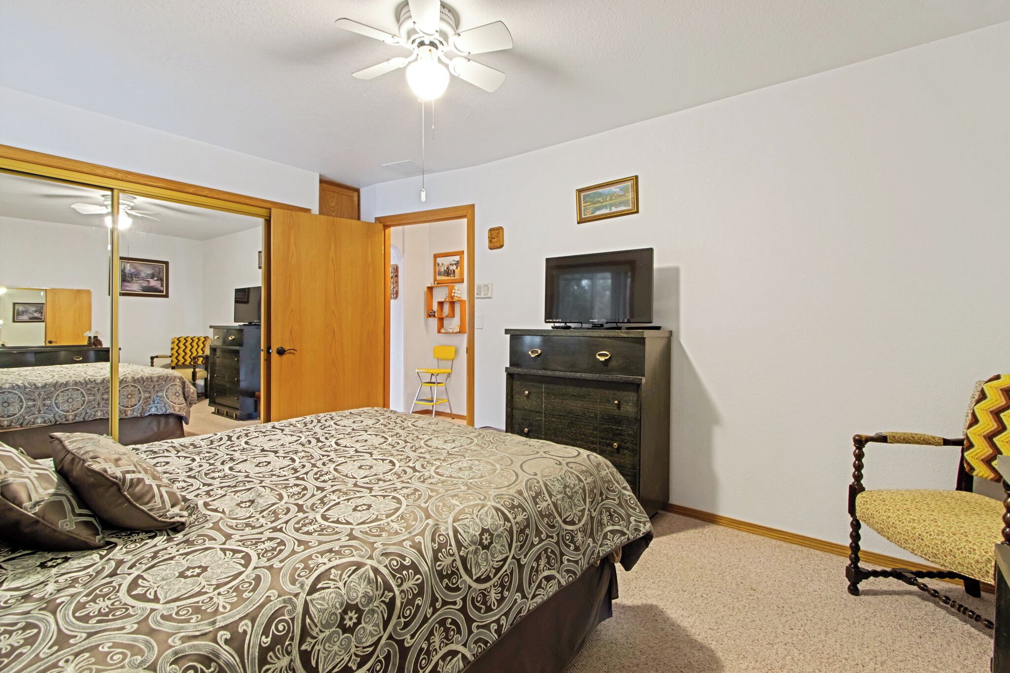 A bedroom with a bed, dresser, chair, television, and a ceiling fan.