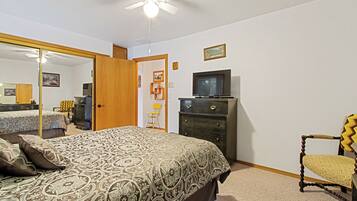 A bedroom with a bed, dresser, chair, television, and a ceiling fan.
