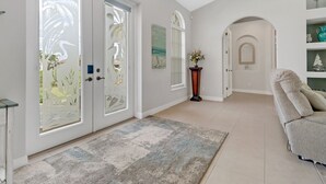 A spacious hallway with a neutral color scheme, a large rug, and a seating area with a sofa. - Cape Ohana 1505 Gulf Access Waterfront Home w/ heated Pool/ Spa & Kayaks (Cape Coral)