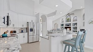 A modern kitchen with white cabinetry, stainless steel appliances, and a marble countertop. - Cape Ohana 1505 Gulf Access Waterfront Home w/ heated Pool/ Spa & Kayaks (Cape Coral)