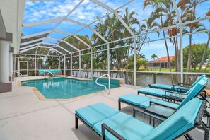 Un espace piscine intérieur avec des chaises longues et une vue sur les palmiers et l’eau.