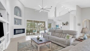 A spacious living room with a large window, a fireplace, a sofa, and a coffee table. - Cape Ohana 1505 Gulf Access Waterfront Home w/ heated Pool/ Spa & Kayaks (Cape Coral)