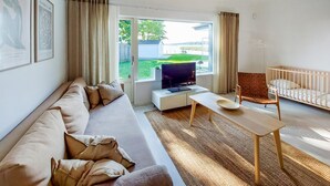 Ein modernes Wohnzimmer mit einer Couch, einem Fernseher, einem kleinen Tisch und einem Babybett.