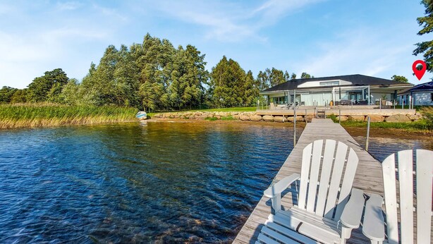 Eine Holzstele, die sich in einen klaren Fluss erstreckt, mit einem modernen Haus im Hintergrund.