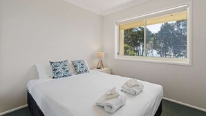 Une chambre d’hôtel avec un grand lit, une table de chevet avec une lampe et une fenêtre donnant sur des arbres.