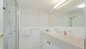 Une salle de bain moderne avec une douche à parois de verre, un lavabo blanc doté d’un plan de toilette en marbre et un grand miroir au-dessus du lavabo.