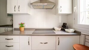 Une cuisine moderne avec des armoires blanches, une hotte en acier inoxydable et un plan de travail sur lequel se trouvent une bouilloire et un panier de fleurs.