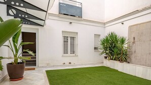 A courtyard with a green lawn, white walls, and potted plants.