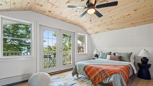 Un dormitorio con una cama grande, dos lámparas de noche, un ventilador de techo y vistas al exterior a través de amplios ventanales.