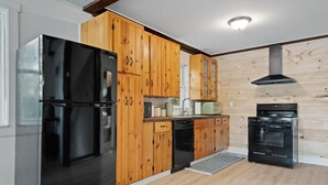Una cocina moderna con armarios de madera, un refrigerador negro, lavavajillas, microondas y estufa.