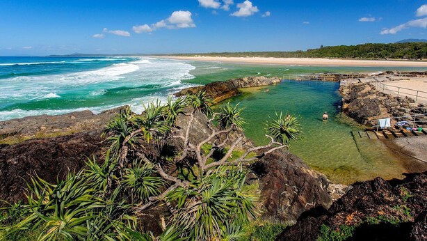 Vista costeira com águas cristalinas, terreno rochoso e uma praia.