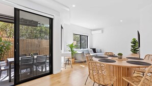 Un espace repas moderne avec une table ronde en bois, des chaises en osier et une porte-fenêtre coulissante donnant sur une terrasse extérieure.