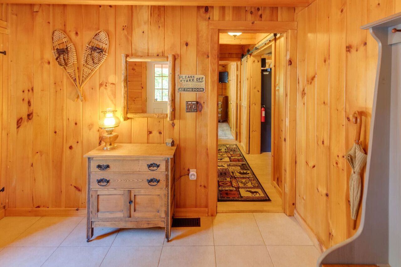 A wooden interior hallway with a wooden dresser, a mirror, and a sign requesting guests to take off their shoes at the door.