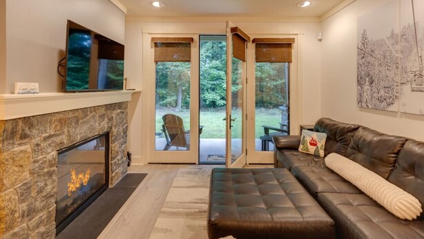A modern living room with a stone fireplace, leather sofa, and a glass door leading to a patio.
