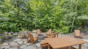 An outdoor seating area with Adirondack chairs and a stone fire pit surrounded by a stone patio.