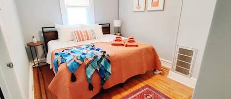 A bedroom with a bed, a nightstand, a lamp, a window, and a red rug.