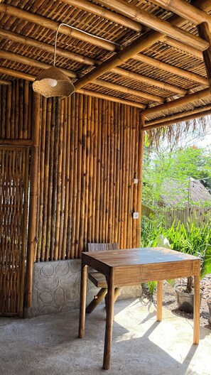 A bamboo structure with a table and chairs, a hanging light fixture, and a stone wall. - elbamboo guesthouse (Banyuwangi)