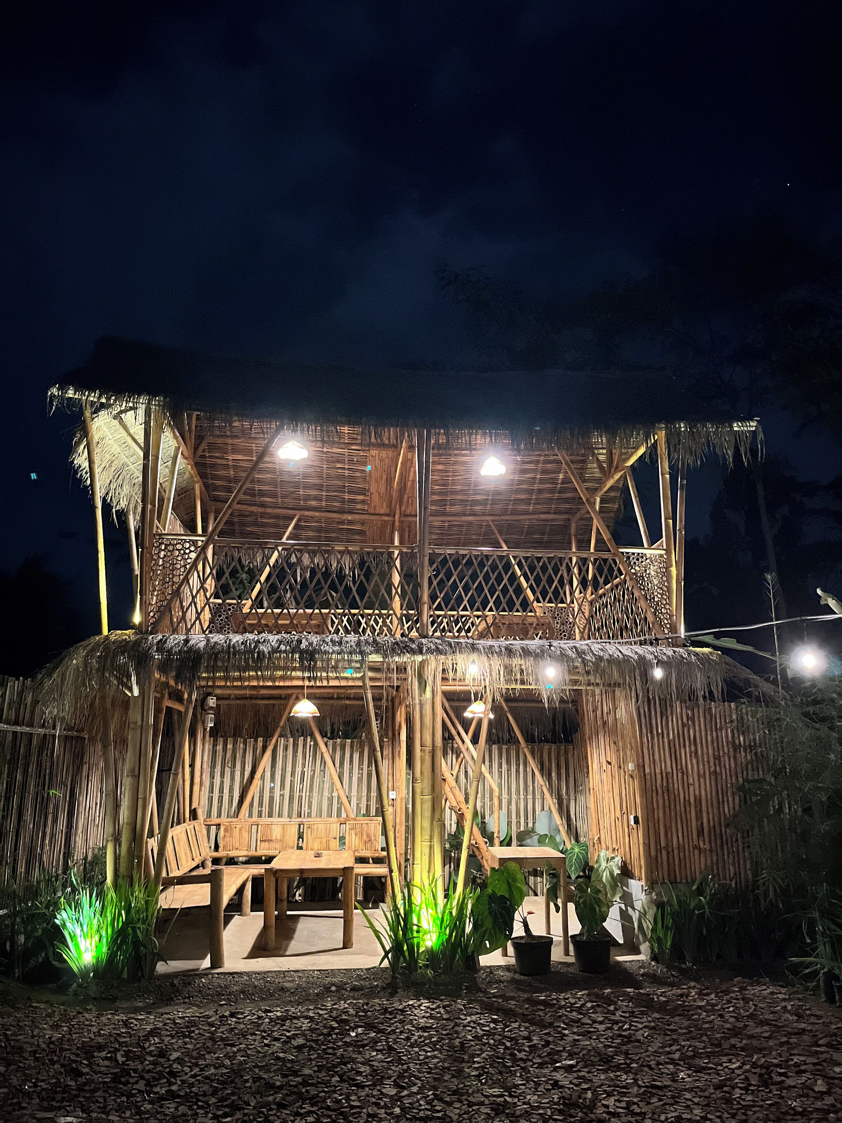 A bamboo structure with a thatched roof, wooden seating, and potted plants.