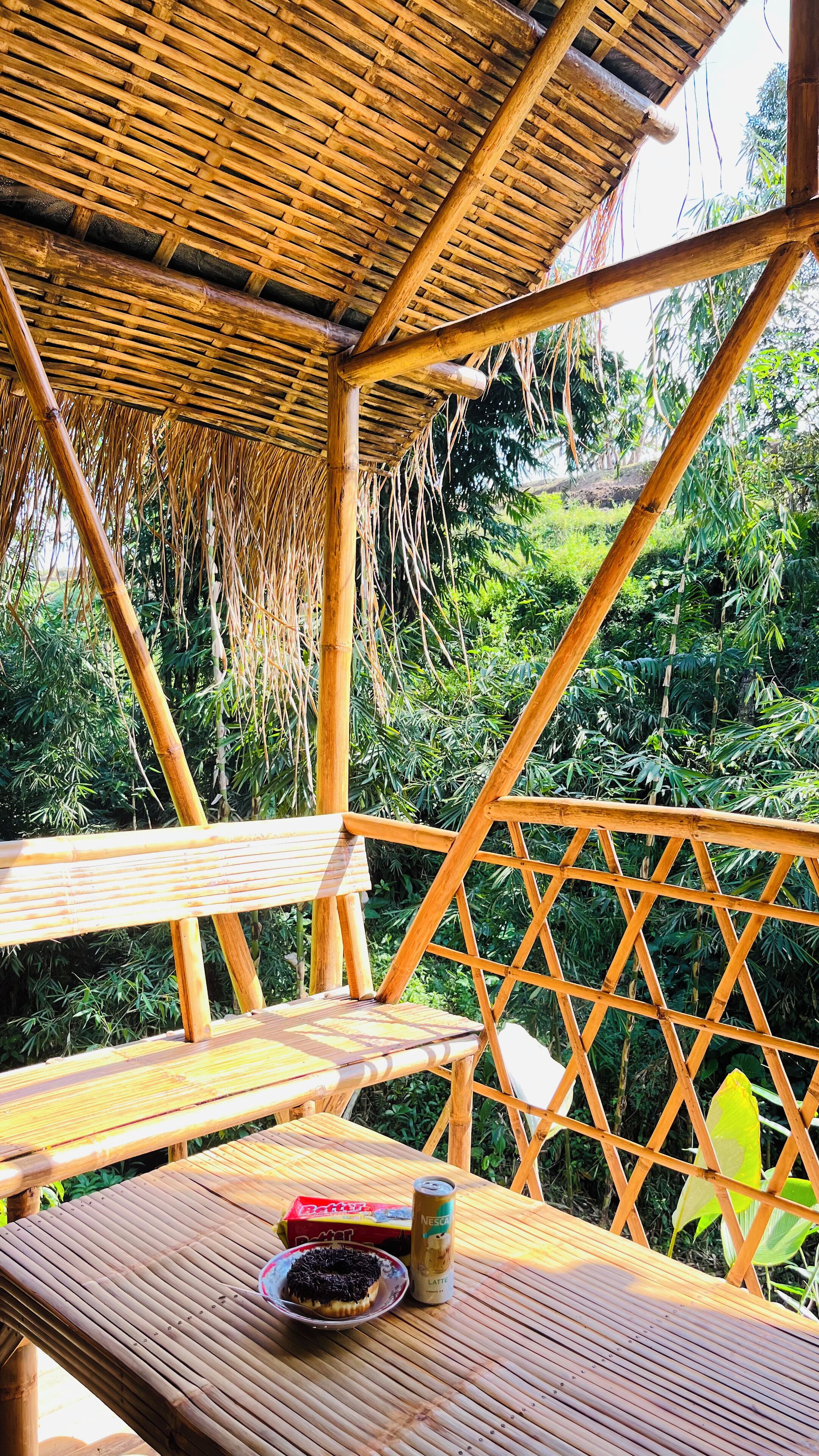 An outdoor wooden deck with a thatched roof, surrounded by lush greenery.