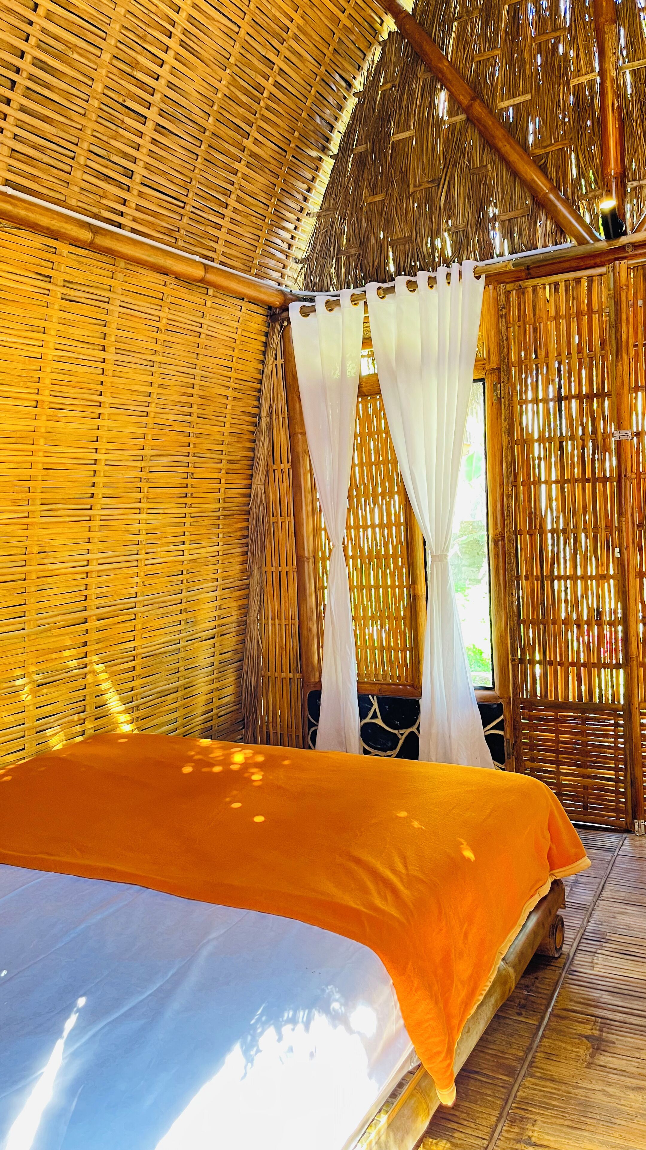 Quarto com cama, cortinas brancas e teto de palha.