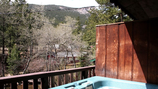 Una terraza de madera con un jacuzzi y vistas a una zona boscosa con montañas al fondo.