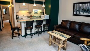 A compact living space with a kitchenette, a brown leather sofa, and a small wooden coffee table. - One Bedroom, Two Bath Condo with River View (Estes Park)