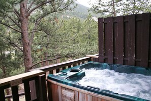 A hot tub with a wooden deck and a view of trees and mountains. - Hot tub suite with full kitchen, patio with river view (Estes Park)