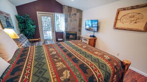 A bedroom with a large bed, a fireplace, a television, and a door leading to a balcony. - Hot tub suite with full kitchen, patio with river view (Estes Park)