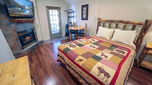 A bedroom with a large bed, a fireplace, a wooden floor, and a door with blinds. - Hot Tub Suite with Gas Fireplace and View from Deck (Estes Park)