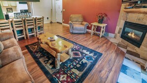 Ein gemütliches Wohnzimmer mit Kamin, Couch, Holz-Couchtisch und einem gemusterten Teppich.
