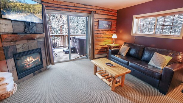 A cozy living room with a fireplace, a leather sofa, and a view of the outdoors through a sliding glass door.