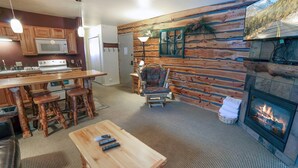 A rustic cabin interior with a kitchen, dining area, and fireplace.