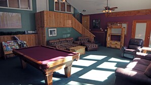 A pool table, a sofa, a chair, a staircase, and a ceiling fan in a room with a wooden floor and walls. - Inexpensive Studio with King bed, Mountain Style decor, and patio with gas grill (Estes Park)