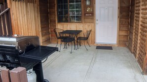 A wooden cabin with a grill, a table with chairs, and a door labeled "Glacier Lily". - Inexpensive Studio with King bed, Mountain Style decor, and patio with gas grill (Estes Park)