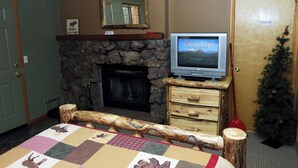A room with a stone fireplace, a television on a wooden stand, a Christmas tree, and a quilt on the bed. - Studio with Full Kitchen, Queen bed, Patio with Personal Grill (Estes Park)