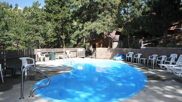 A swimming pool with a diving board, surrounded by white plastic chairs and a stone wall.