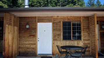 A wooden cabin with a white door, a window with a grid pattern, and a patio with a table and chairs.