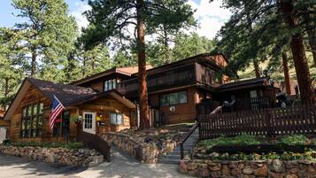 A log cabin with a stone staircase, wooden deck, and a flag.