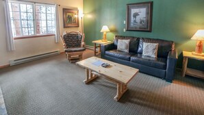 A living room with a green wall, a leather sofa, a wooden armchair, a coffee table, and two side tables with lamps. - Mountain style one bedroom with fireplace (Estes Park)