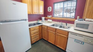 A compact kitchen with wooden cabinets, a white refrigerator, a microwave, and a dishwasher. - Mountain style one bedroom with fireplace (Estes Park)