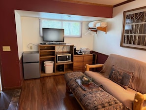 Un espacio habitable compacto con sofá, televisión, microondas y un refrigerador pequeño.