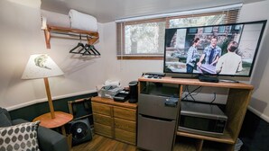 Ein kleiner Wohnraum mit Fernseher, Holzmöbeln, einem Ventilator und einem Kühlschrank.